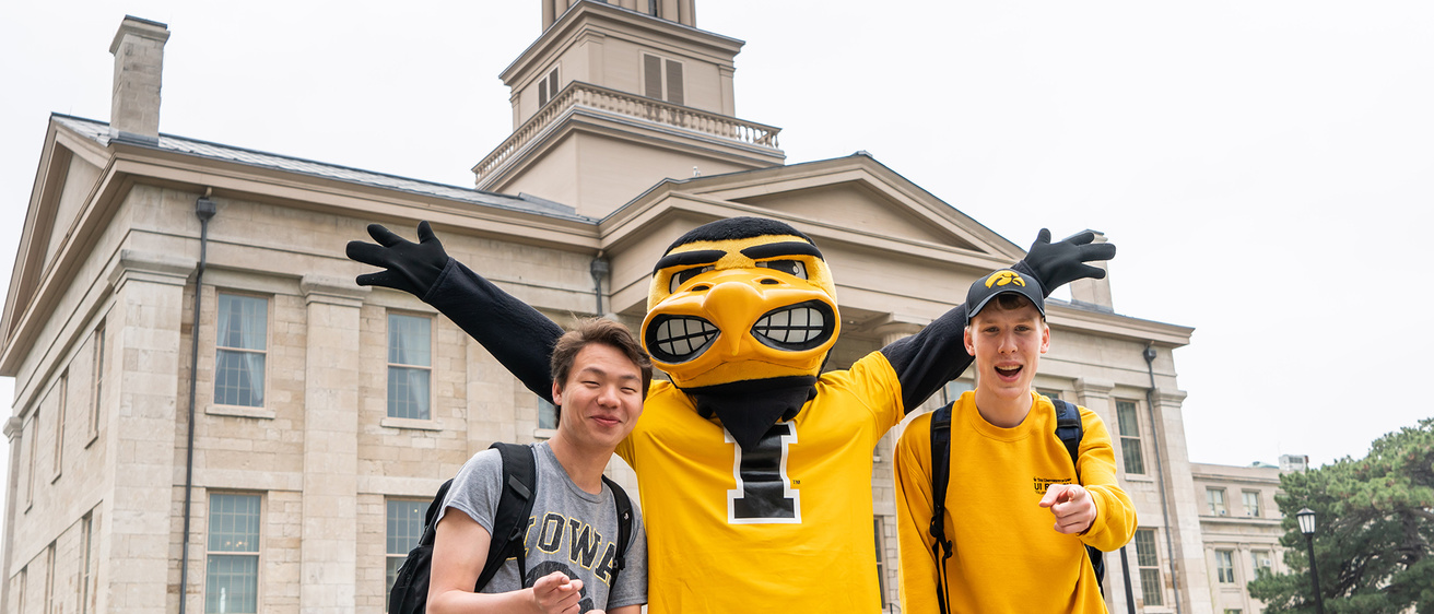 Herky with two male students in front of Old Capitol