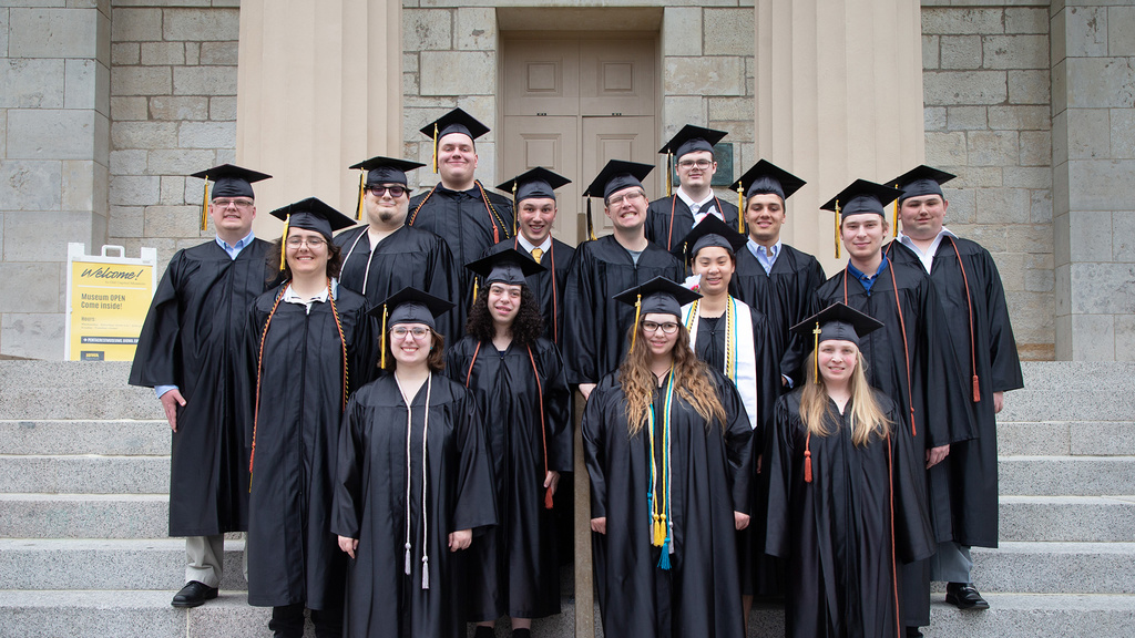 Students in graduation cap and gowns standing on stone stairs